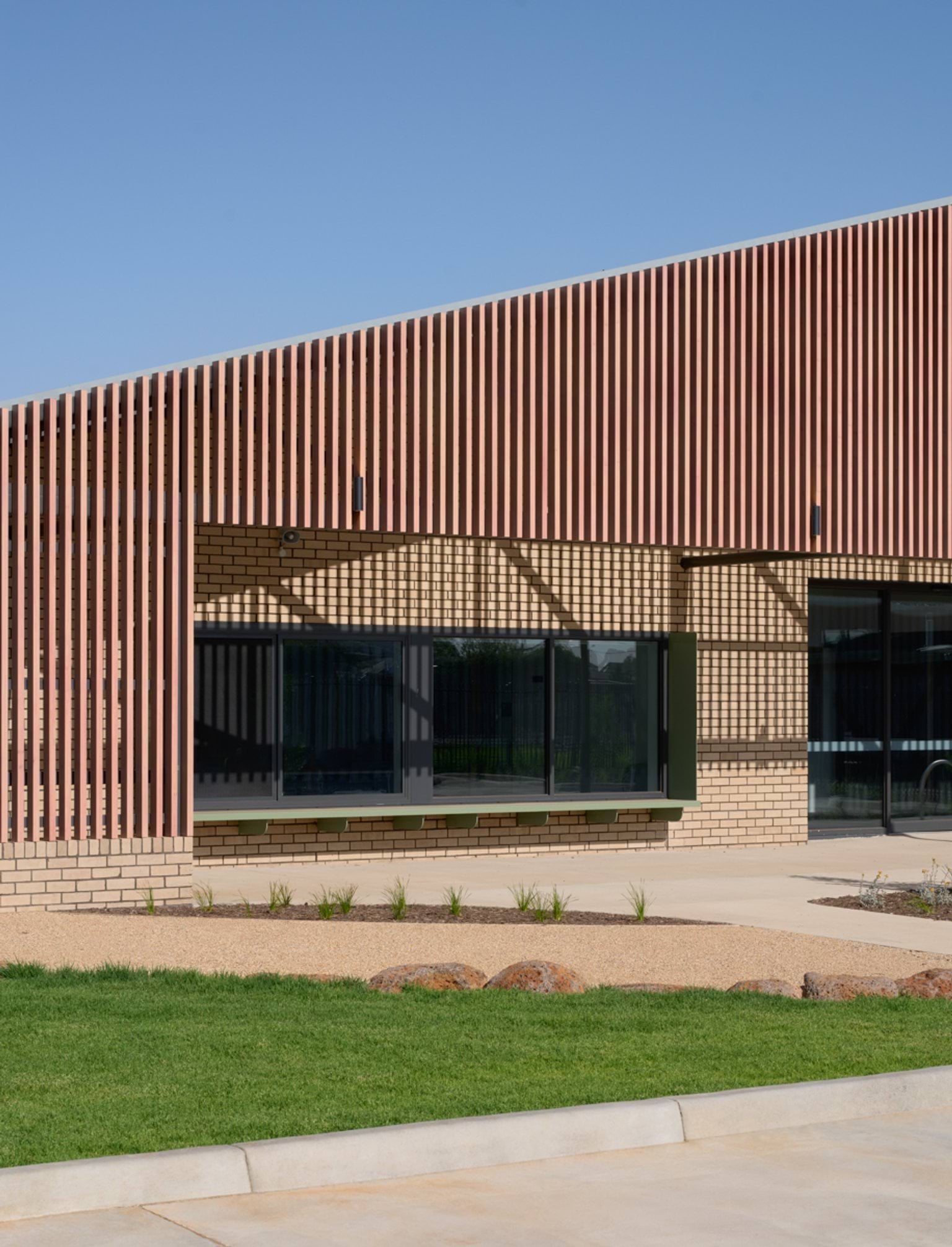 A close view of the slatted timber façade over windows on the building’s front, with lawn and native plantings in the foreground.
