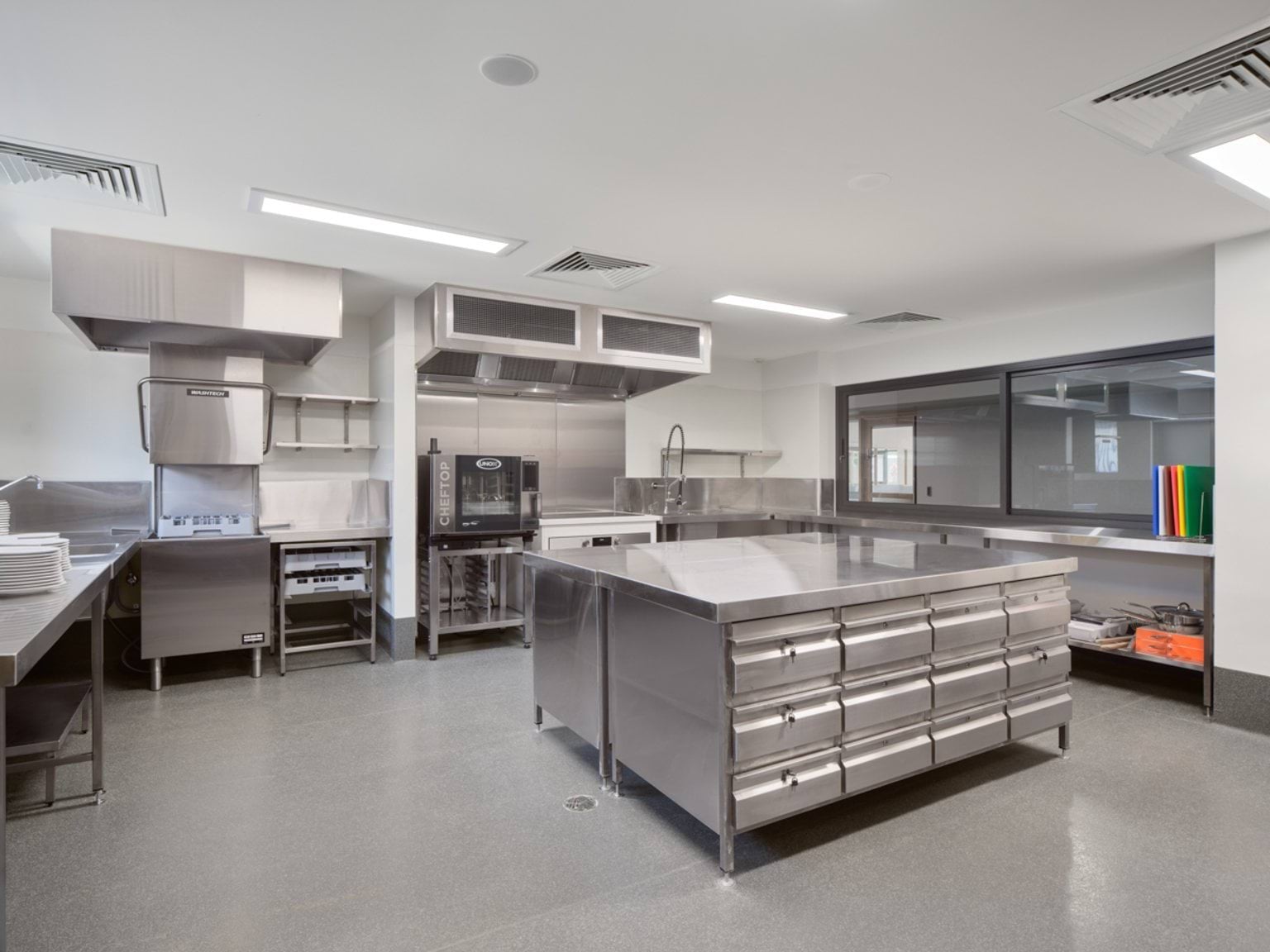 A commercial‑style kitchen with stainless steel benches, appliances, and storage drawers for meal preparation.