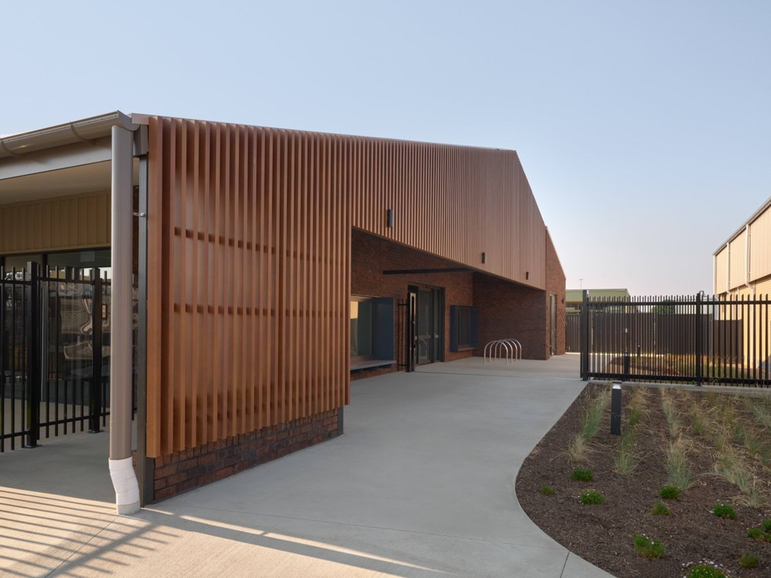 An exterior view of an early learning centre entrance with timber‑screen cladding, paved pathways, and landscaped planting.