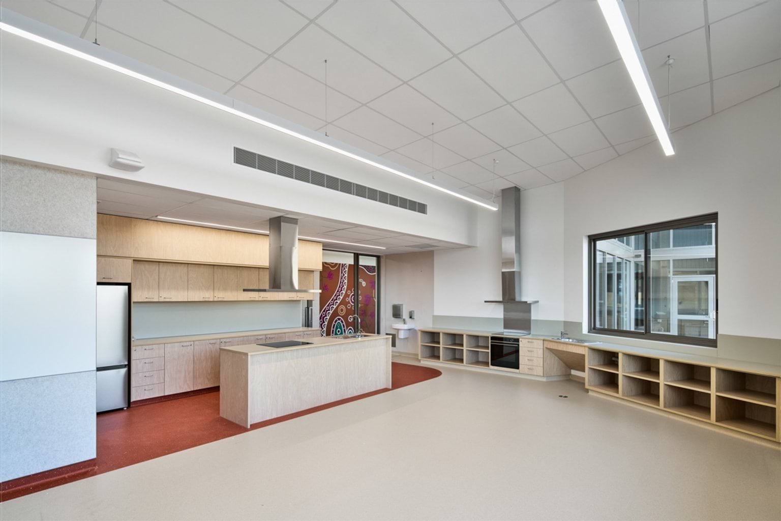 A light‑filled teaching kitchen with extensive bench space, storage cabinetry, two oven units, and a central island.
