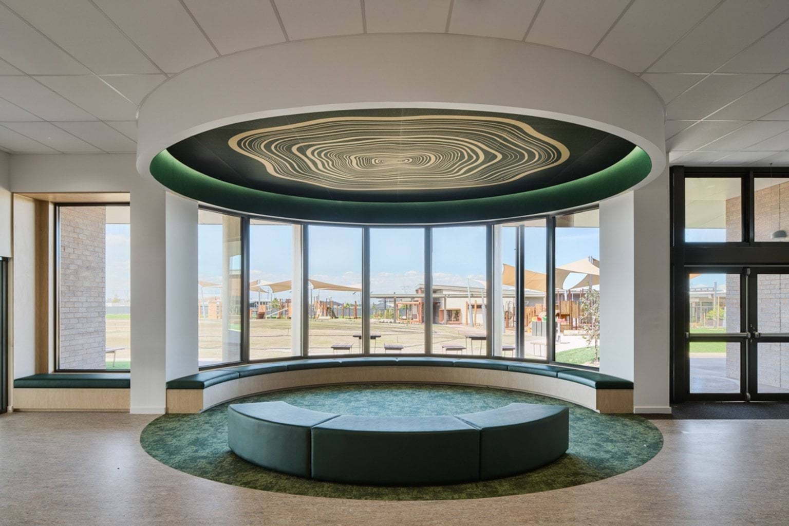 An indoor gathering space with circular seating, large windows, and a feature ceiling with concentric artwork.