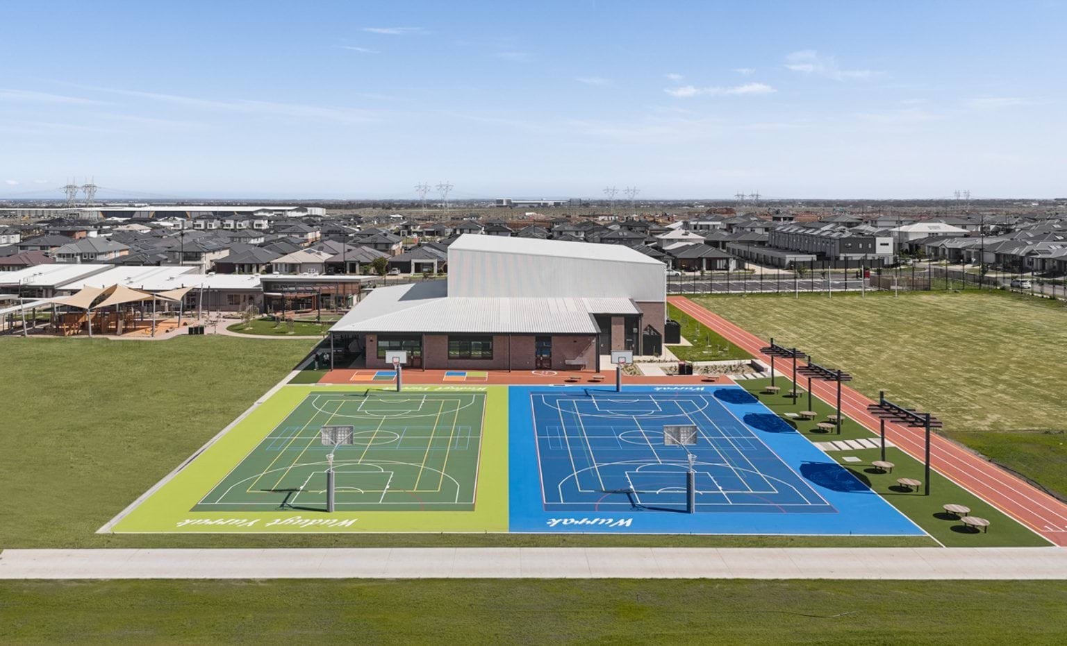 An elevated view of the sports courts, running track, and main building set within a large open grassed area.