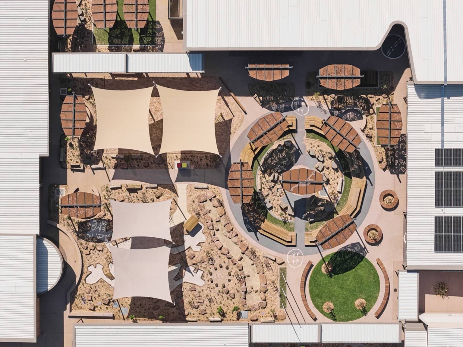 An outdoor courtyard with timber benches, plantings, and multiple patterned shade structures.