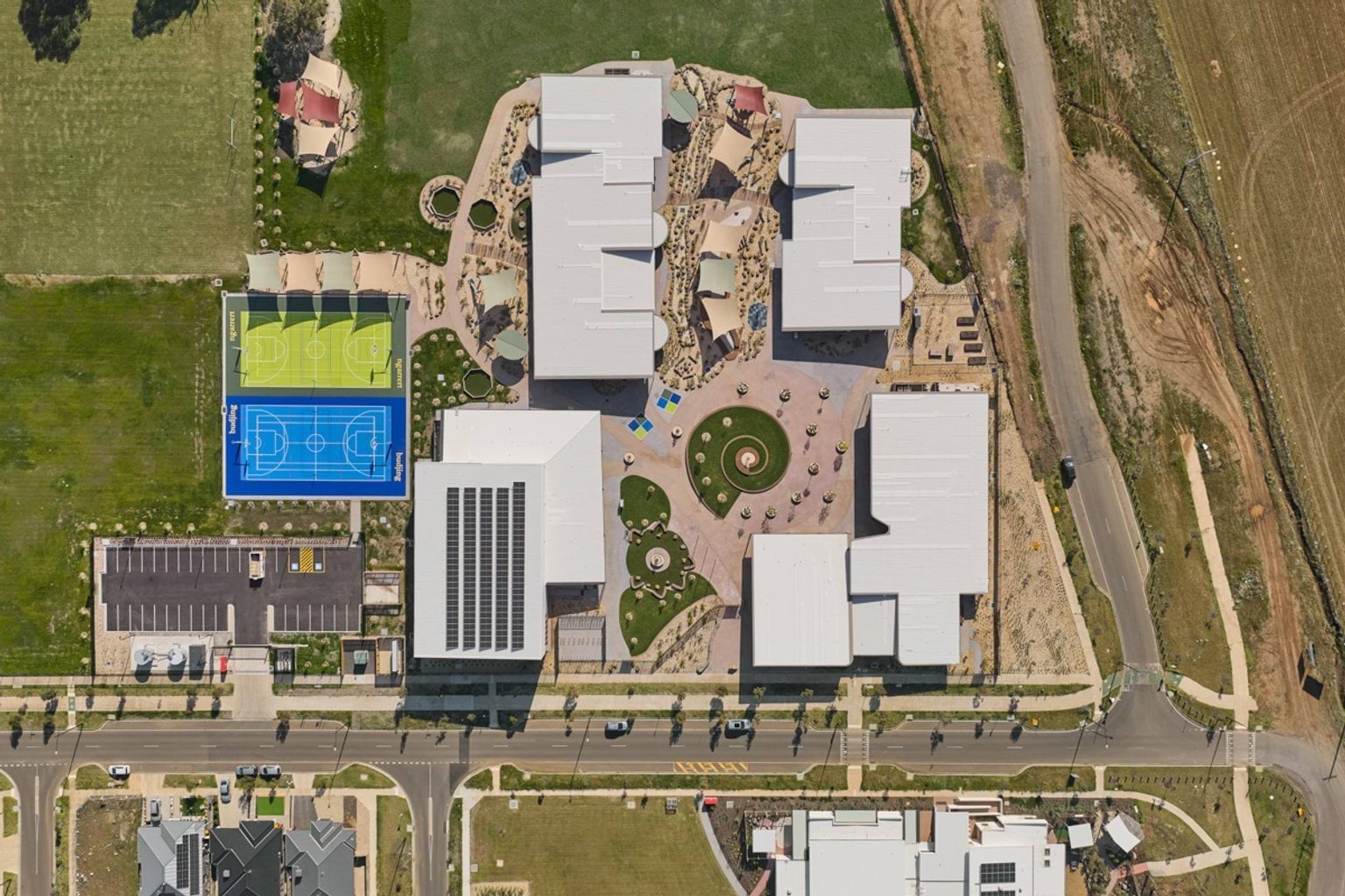 An aerial view of the school showing multiple buildings, landscaped play areas, a central circular courtyard, outdoor courts, and surrounding streets.