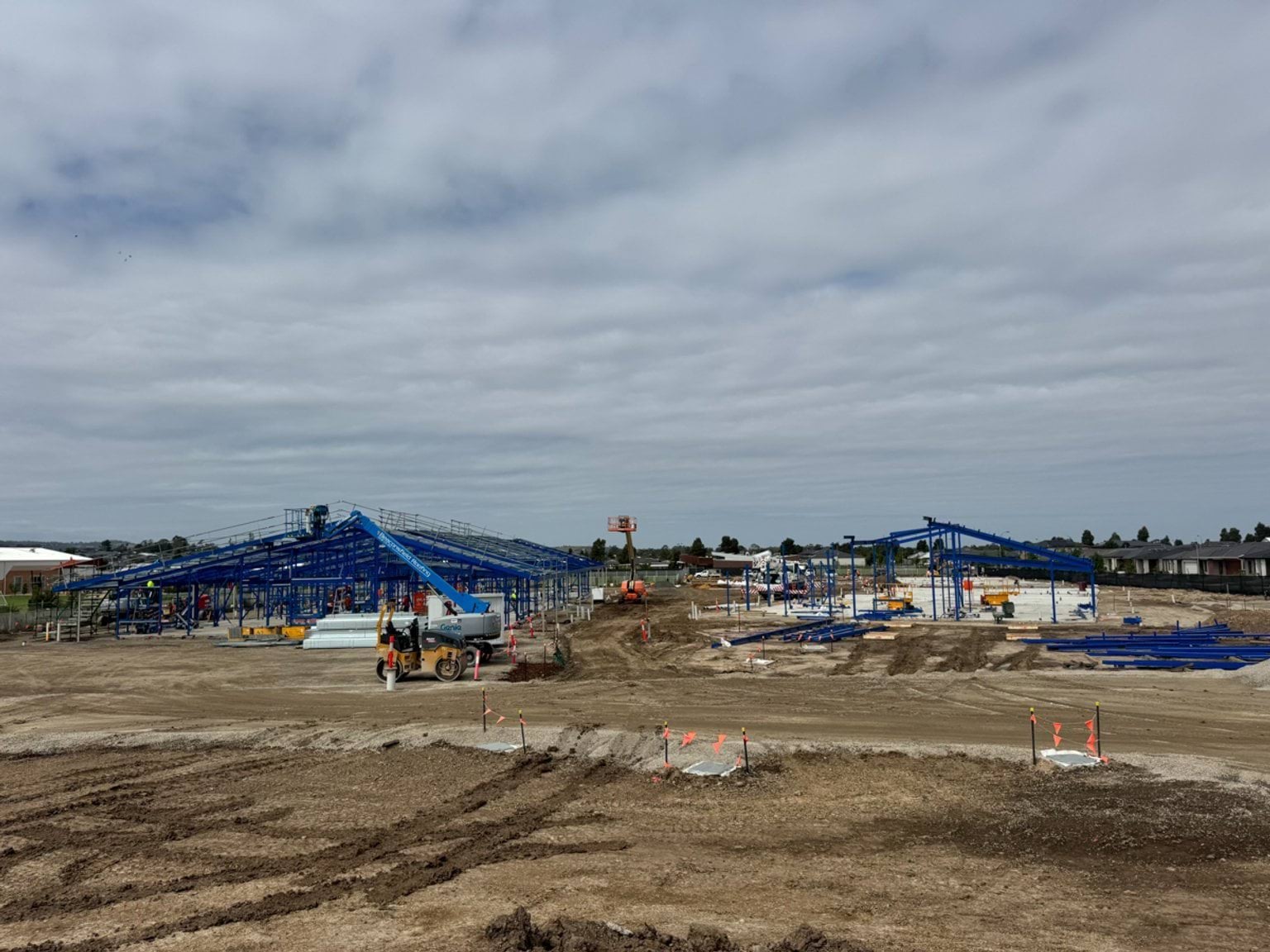 A wide view of the school construction site showing multiple steel-framed buildings being assembled across the cleared land.