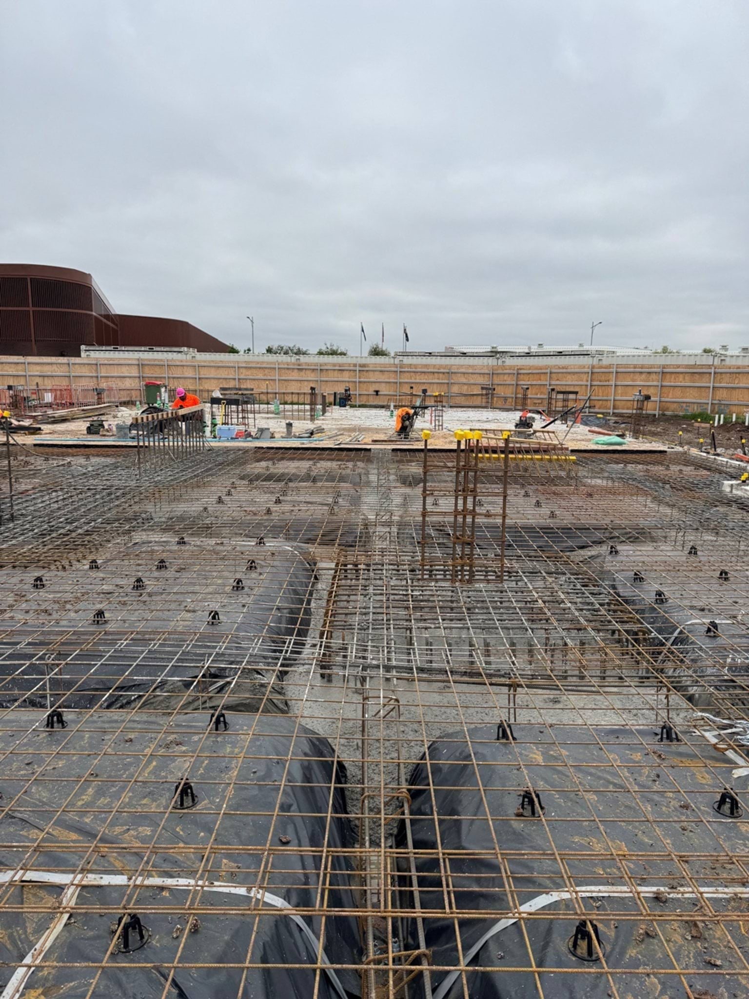 Reinforcement steel laid out across a large construction site, with workers preparing the foundation under an overcast sky.