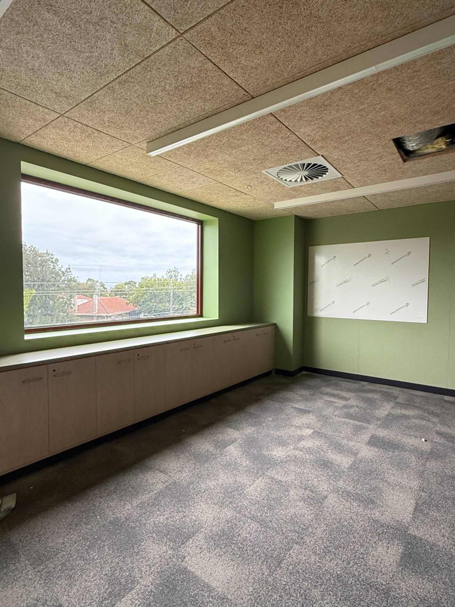A bright classroom with green feature walls, built‑in cabinetry, and a large window overlooking nearby houses and trees.