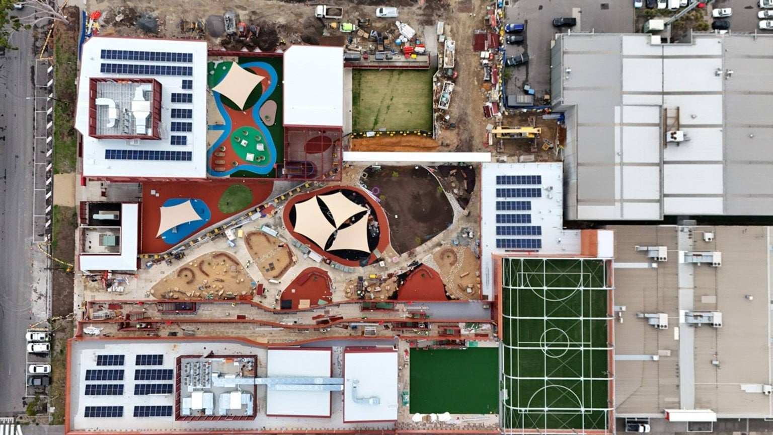 Aerial view of the school campus showing completed buildings, colourful outdoor play areas, shade structures, and landscaped spaces.