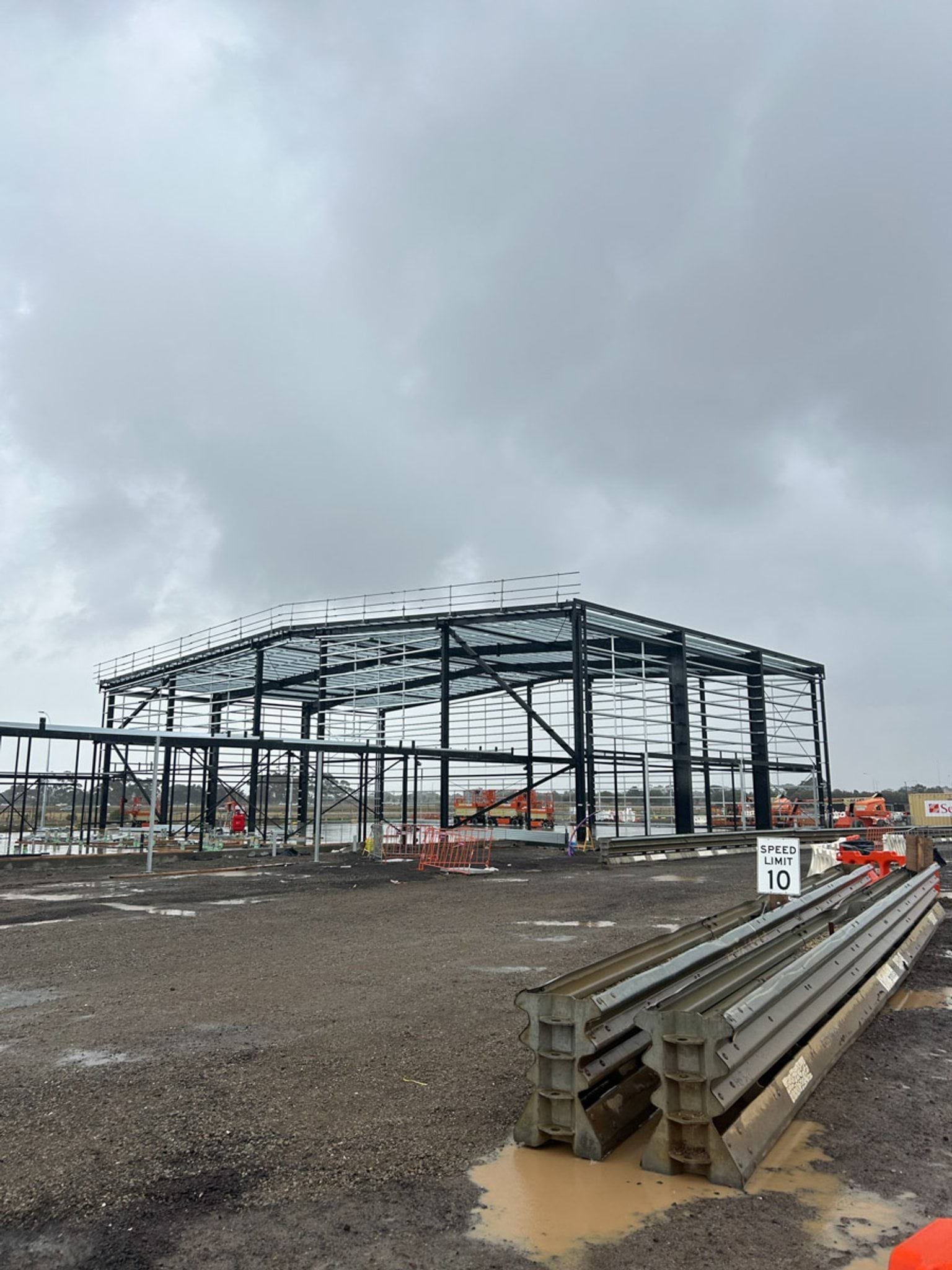 A large steel framework forming part of a school building, with stacked materials and safety signage visible on site.