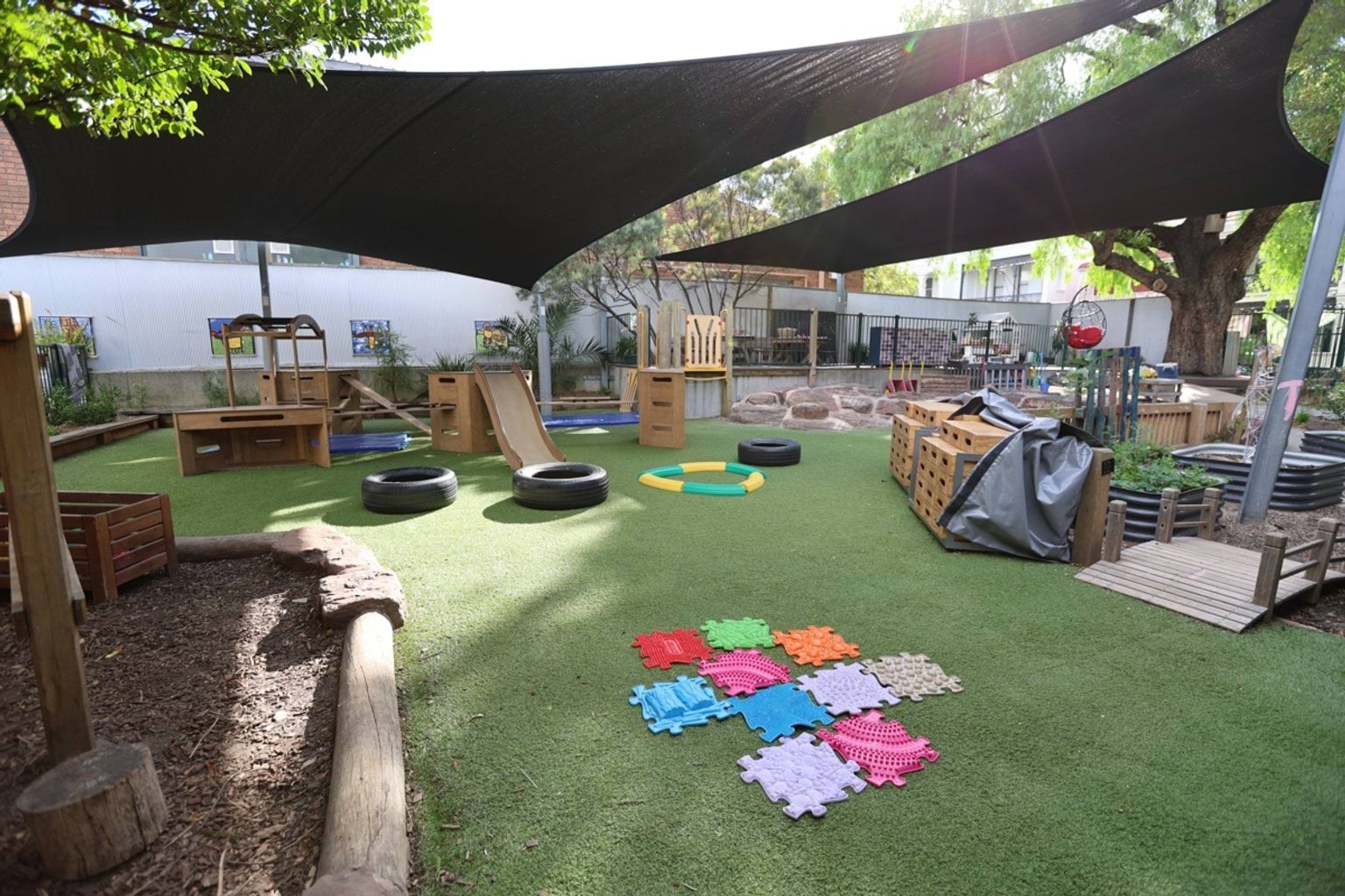 Outdoor play space with shade cloths, play equipment, and turf.