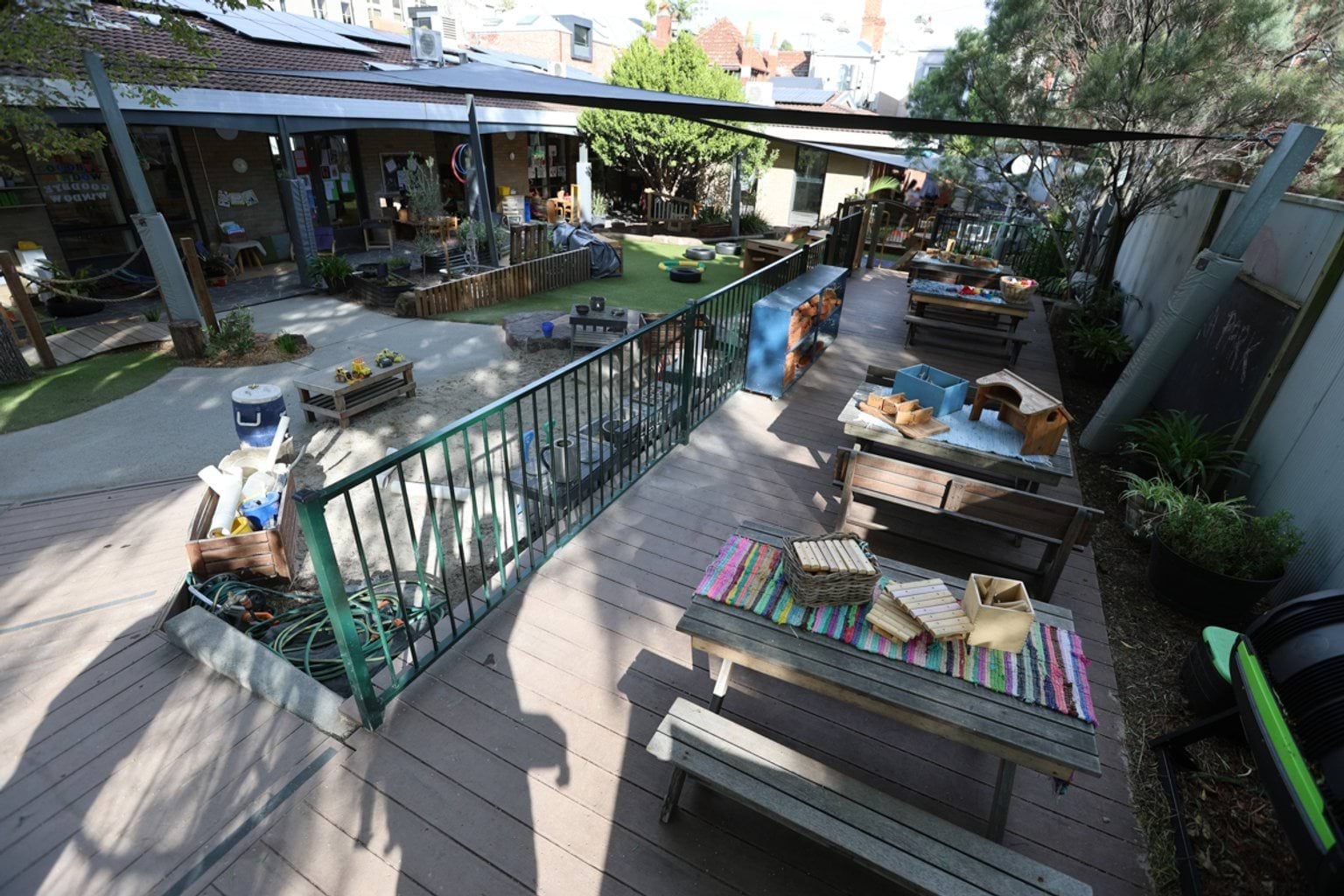 Wide view of an outdoor learning and play space with sandpit, timber tables, loose materials and shaded decking.