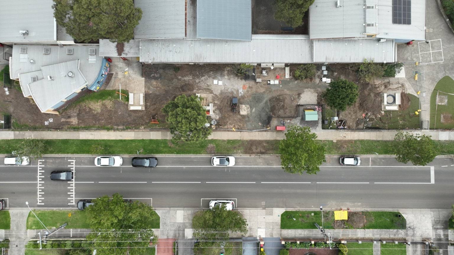 High‑angle aerial view of school buildings with an active construction zone along the street boundary.