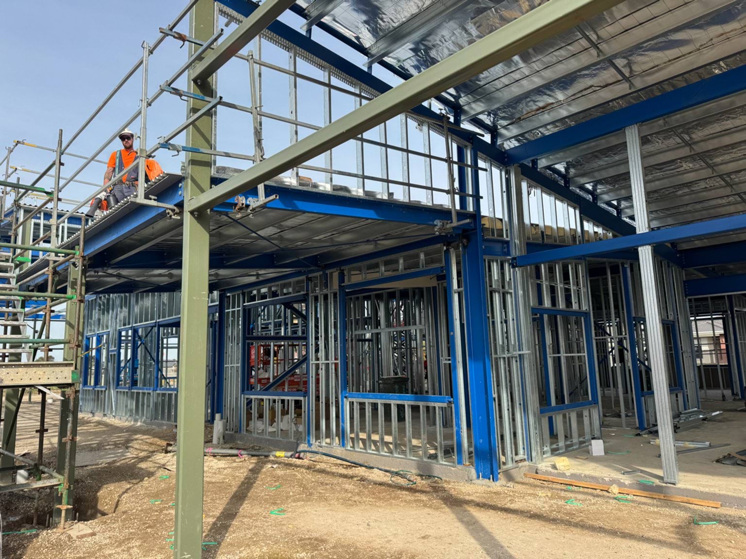 Construction worker on scaffolding within a steel‑framed school building under construction.