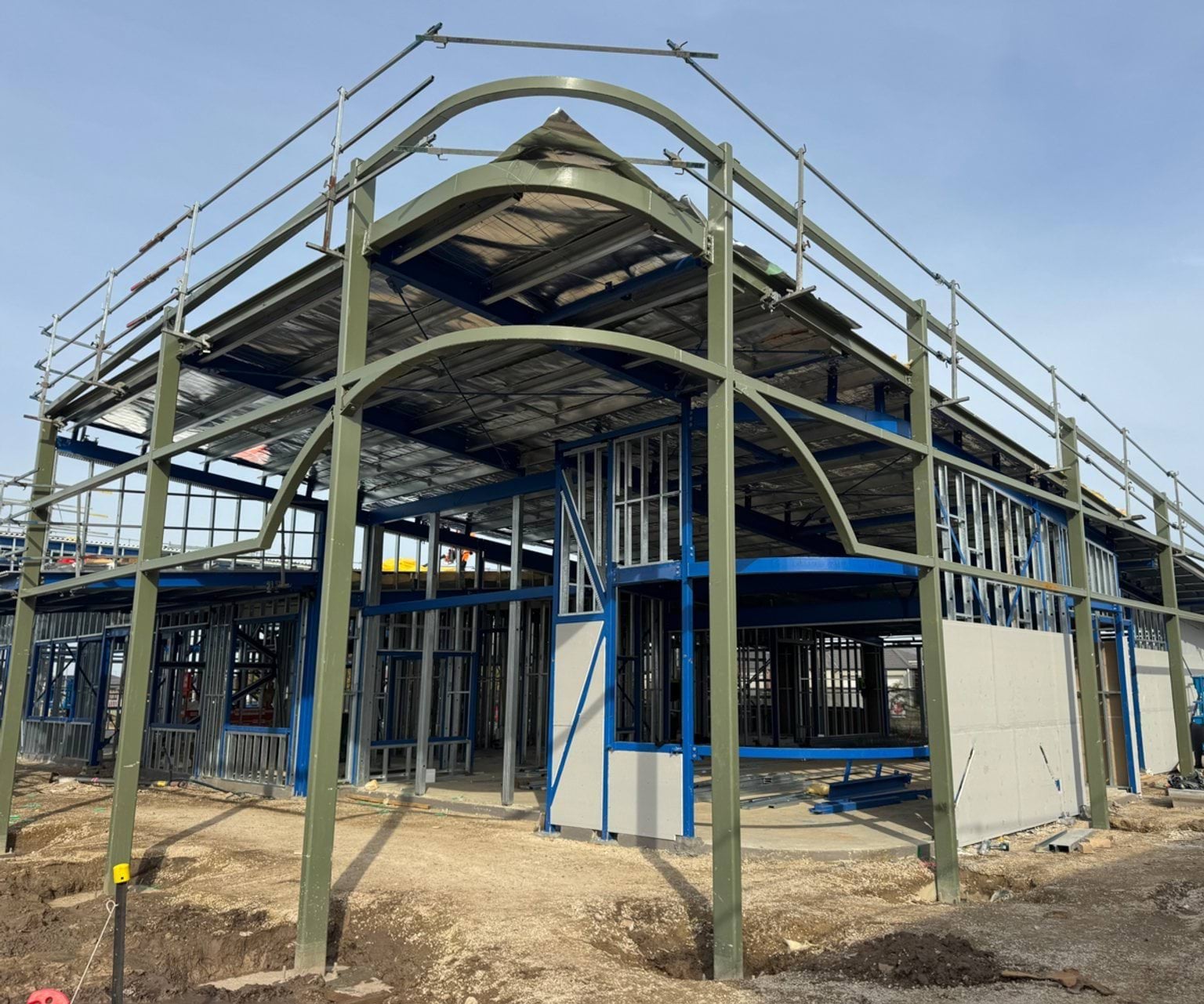 Two‑storey school building under construction with steel framing, curved beams and scaffolding in place.
