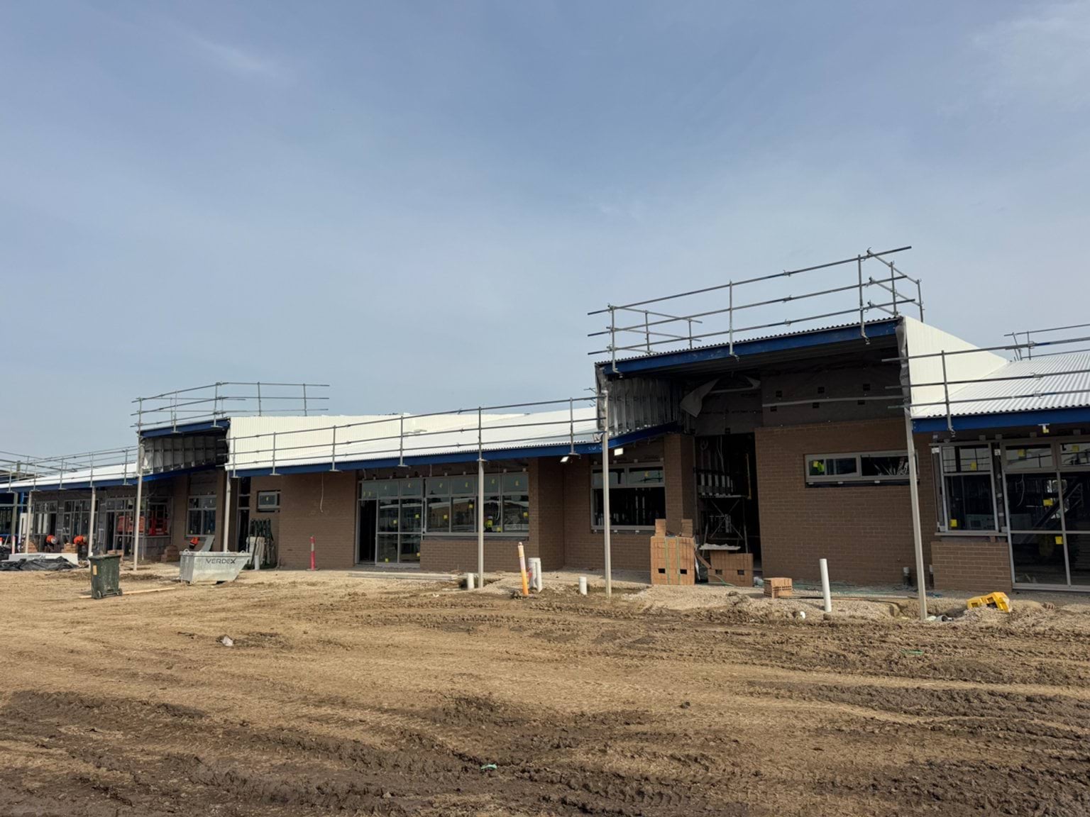 Single‑storey brick classroom block under construction with roofing, windows and scaffolding along the façade.