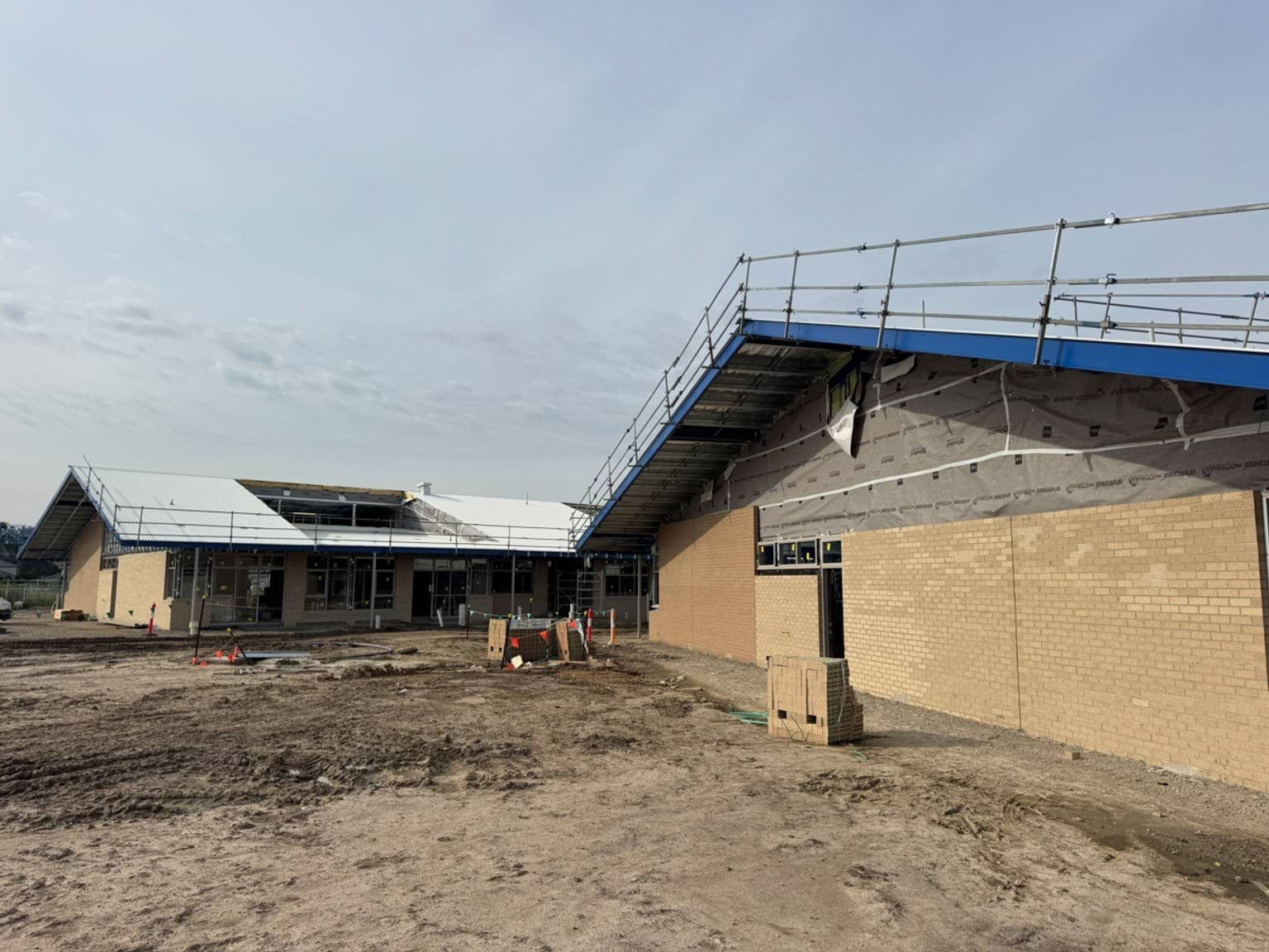 School building exterior showing brick walls, roof installation and unfinished ground works.