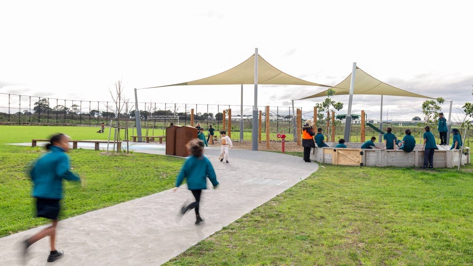 Students running on pavement toward group seated near playground