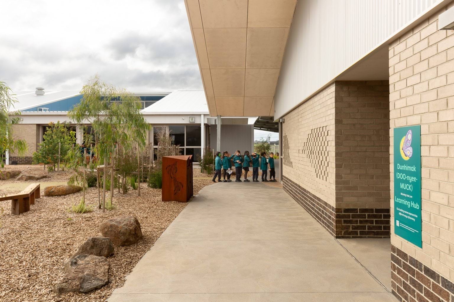 Students queuing outside building on footpath with garden