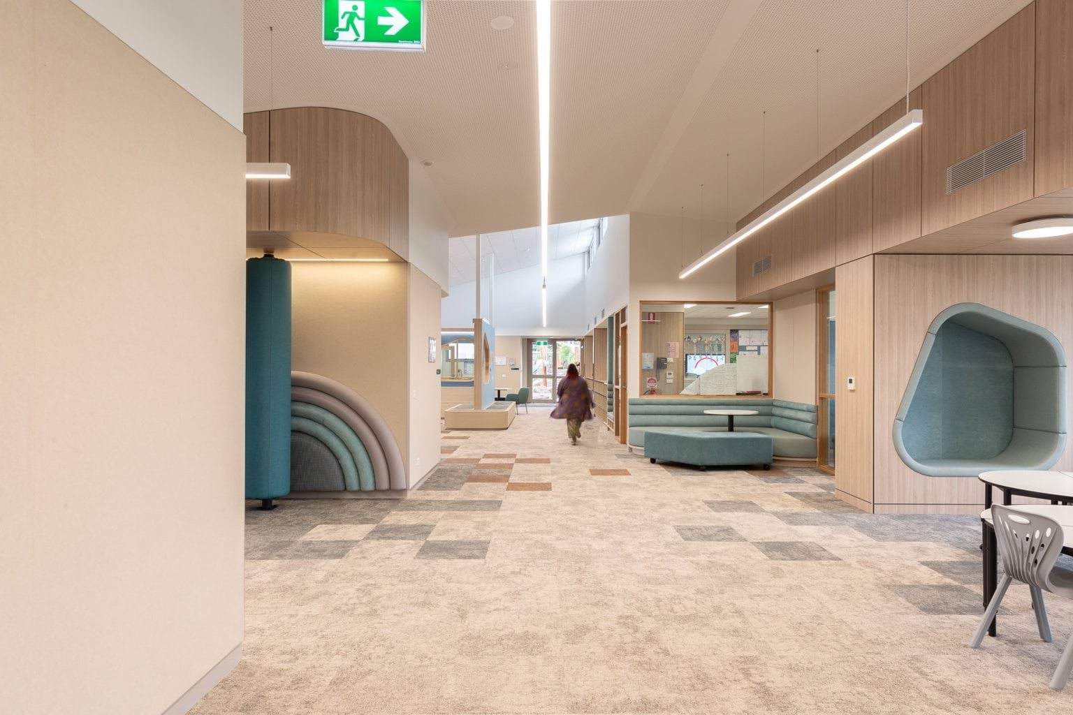 Teacher walking through light blue and cream hallway with various seated areas 