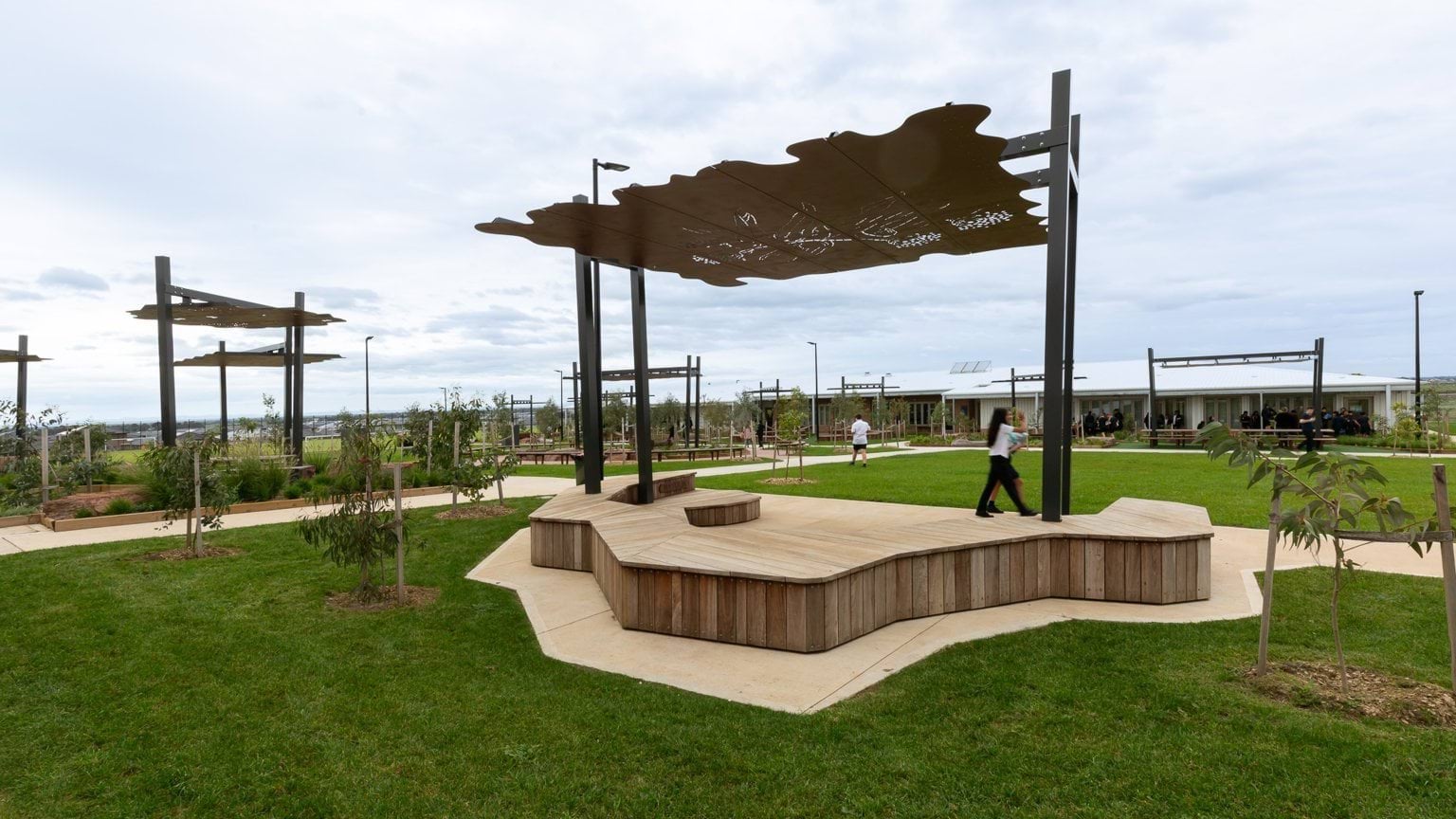 Students walk through grass area with sheltered benches