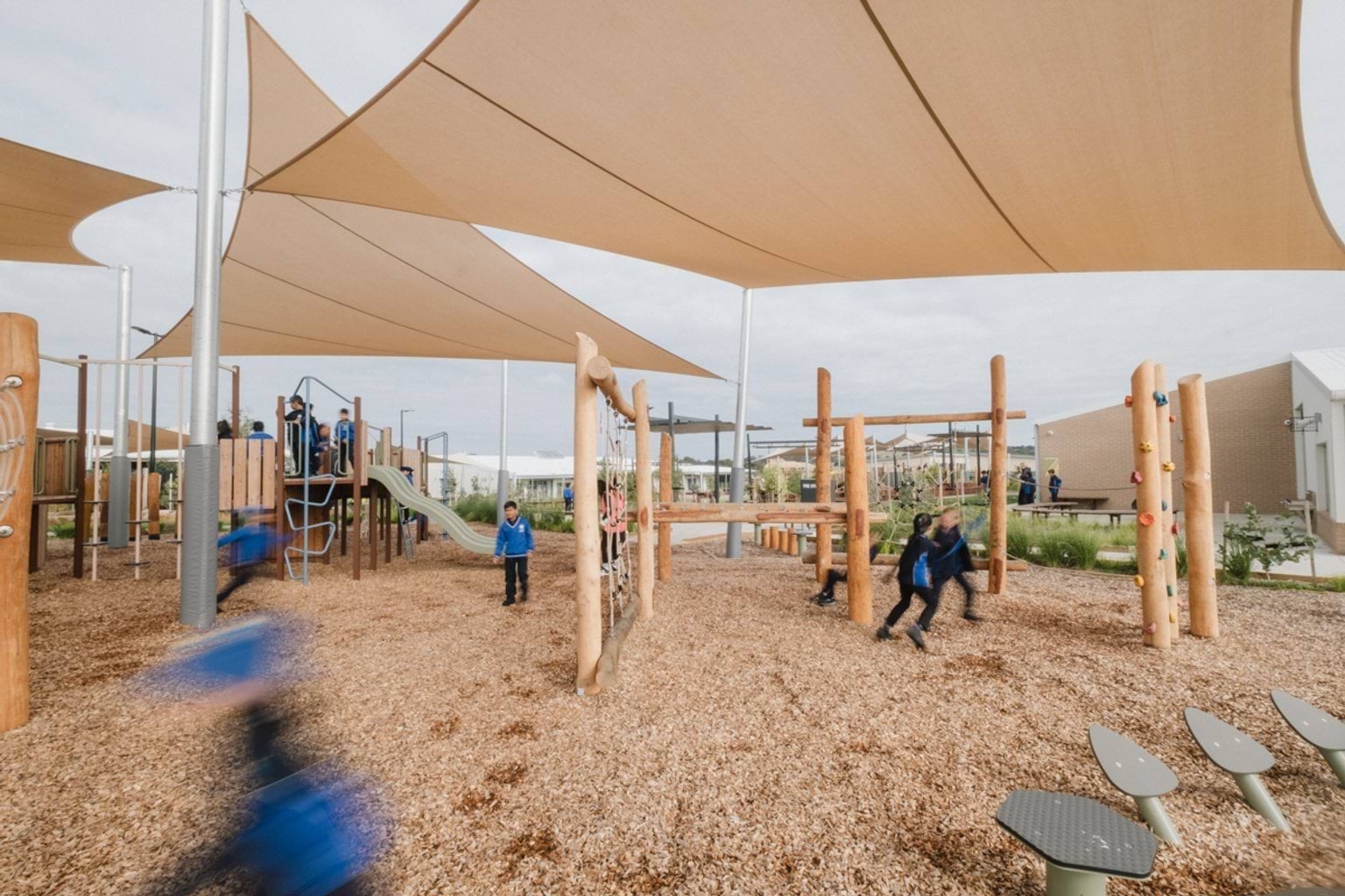 Outdoor sheltered playground area with tanbark. We can see students running throughout.