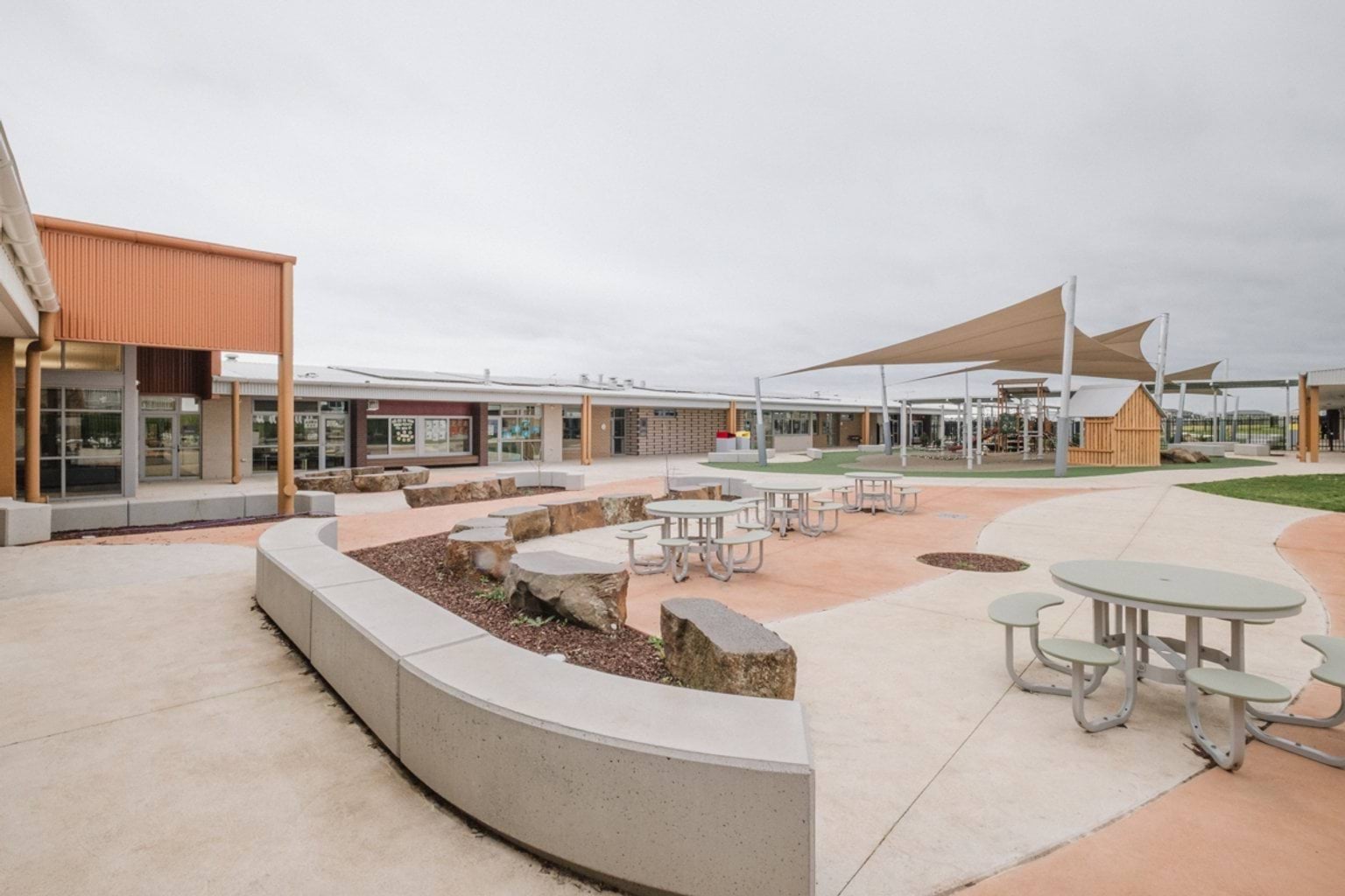 Outdoor paved area with tables and benches. We can see a covered play area in the rear of the space