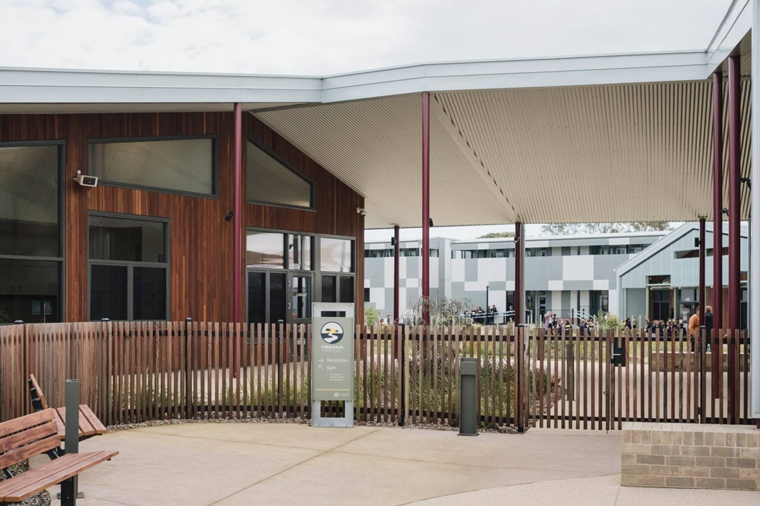 Paved entrance to school building with wooden fence and large covered area above wooden panelled building