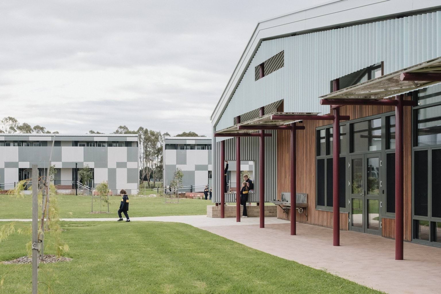 Grass area surrounded by school buildings. We can see new trees planted and a student walking along the footpath