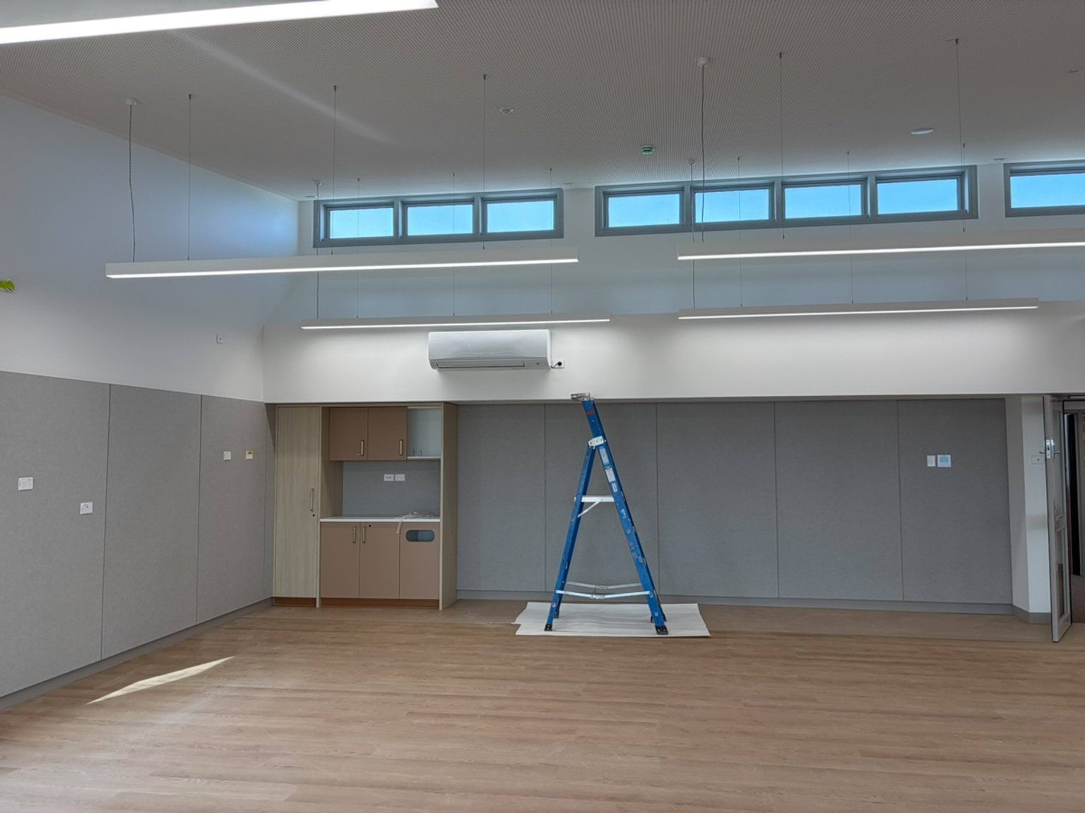 A near-completed room with timber flooring, high windows, grey walls and a ladder