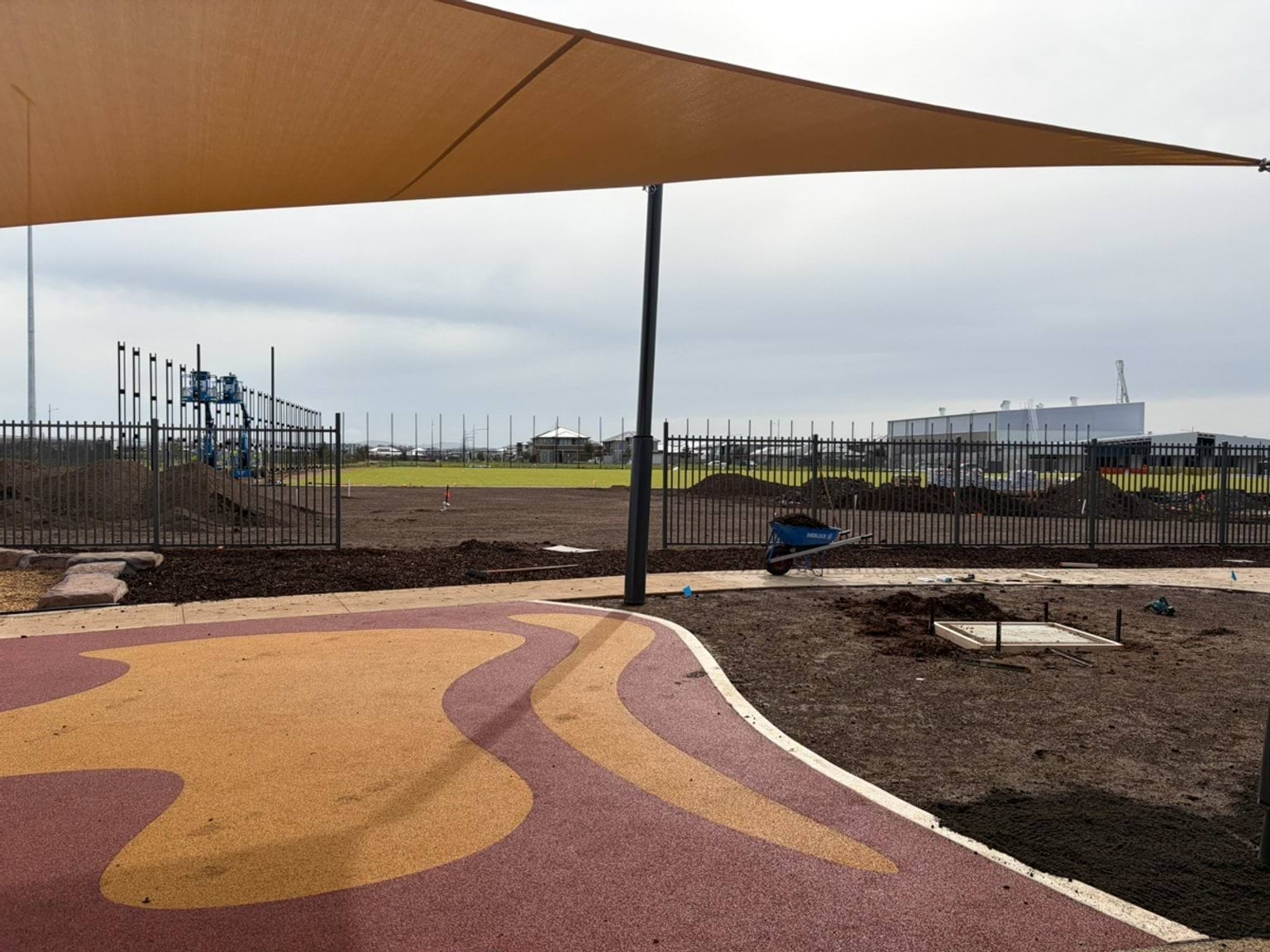 An outdoor play area with colourful safety surfacing, shade sails, landscaping works and fencing around the perimeter.