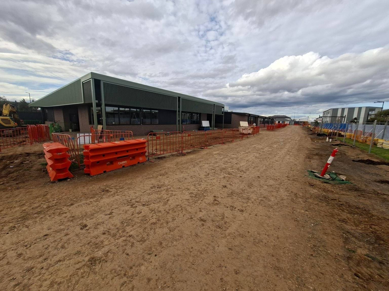 Unpaved road with orange fencing and green building in the background