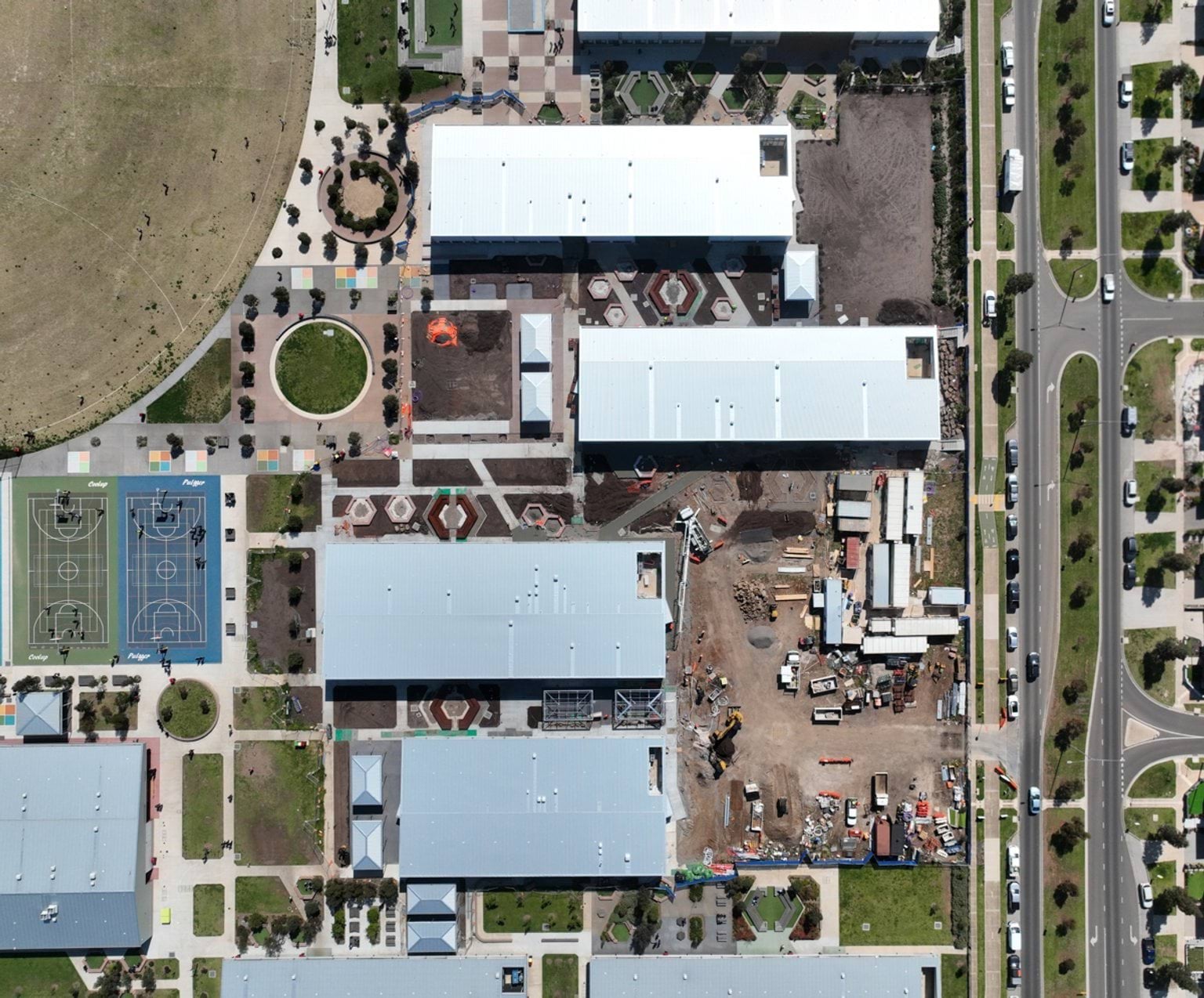 A bird’s-eye view of a school site showing several buildings, landscaped outdoor areas, sports courts and construction works in the centre of the campus.