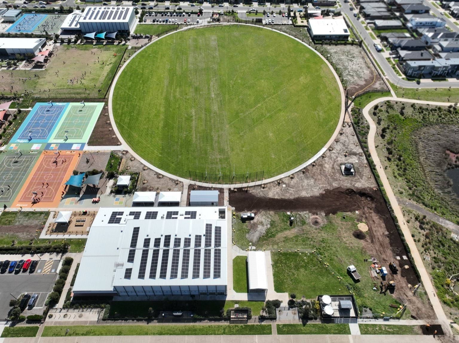An aerial view of a school campus with a large oval sports field, outdoor courts and school buildings. Paths and roads surround the campus..