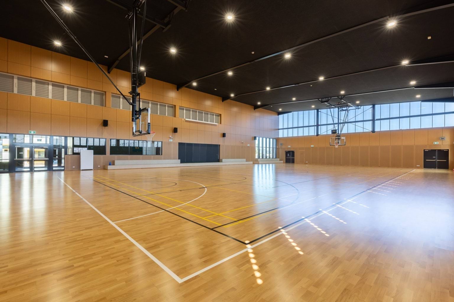 Indoor sports stadium with floorboards, large windows and black roofing