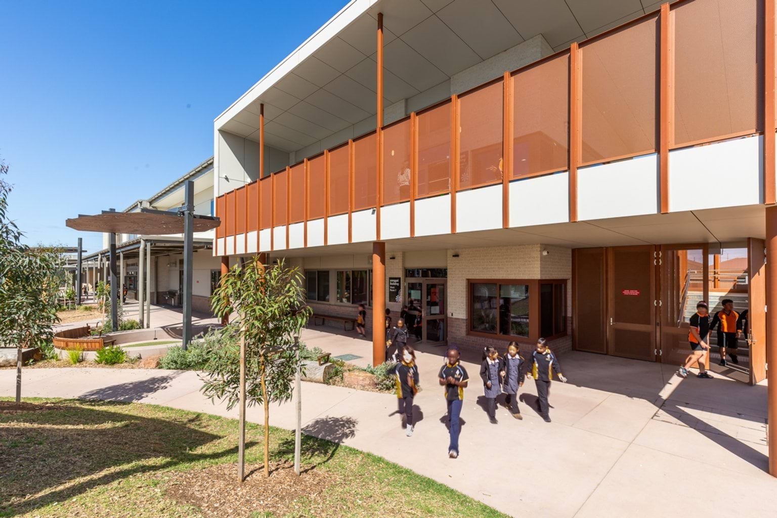 Multi-level school building with walkway underneath, green spaces and landscaped garden beds.