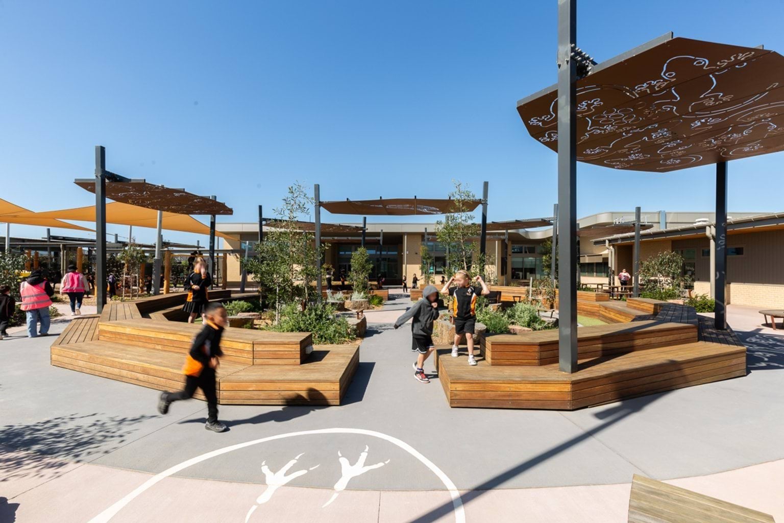 Large, paved yarning circle with curved wooden benches, garden beds and outdoor shelters.