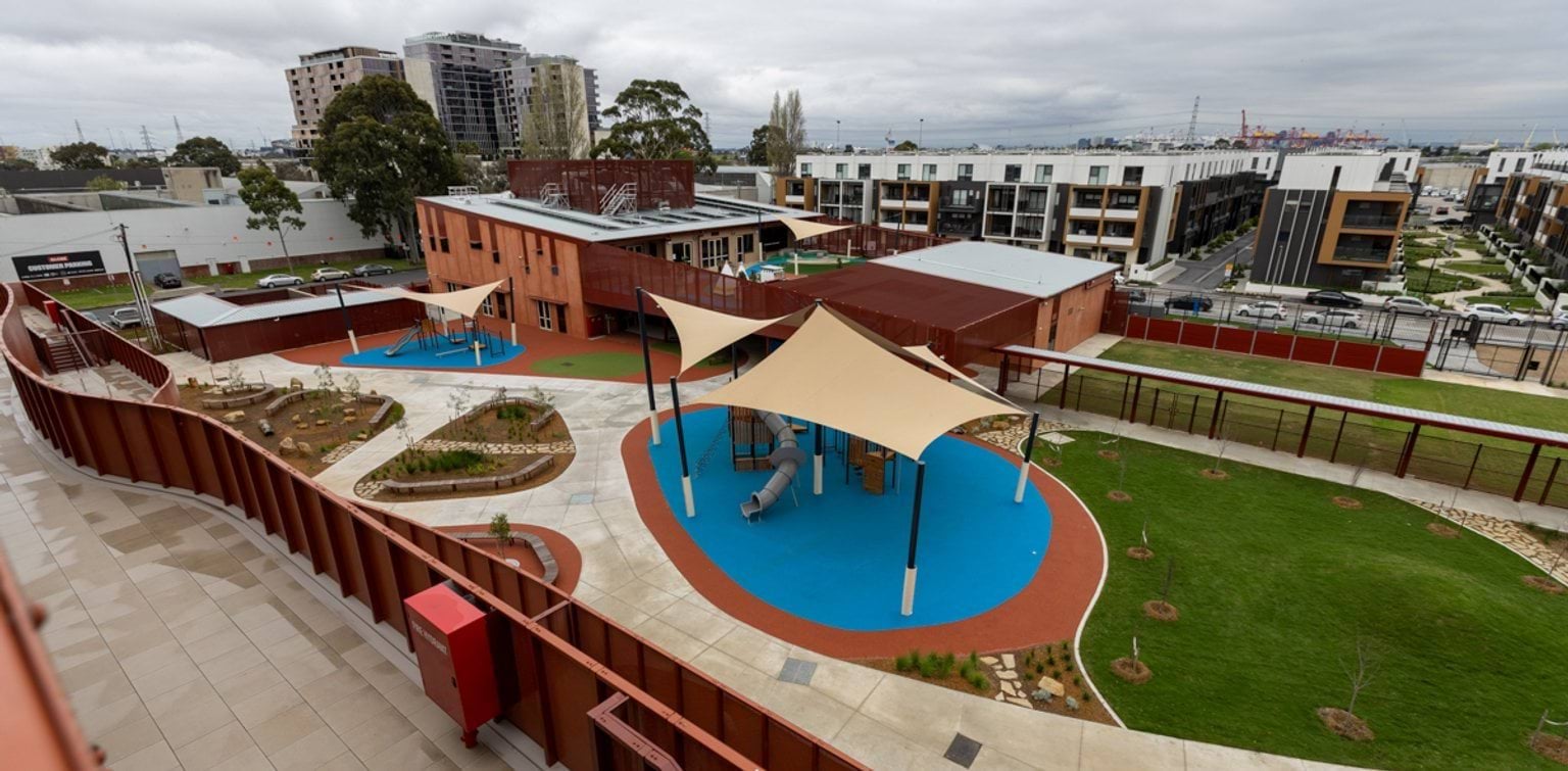 Above view of outdoor play areas, green spaces and landscaped gardens with the school building in the background.