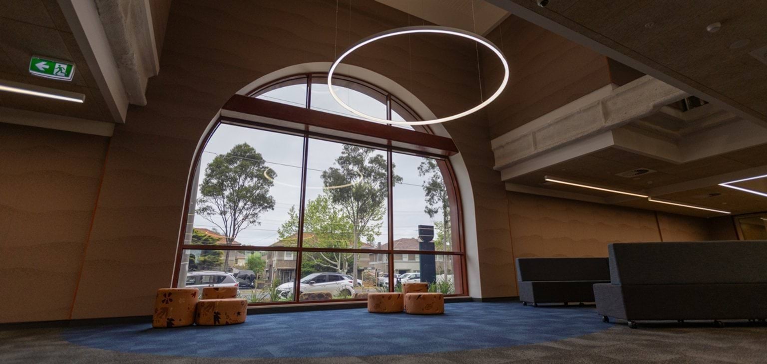 An open foyer area with seats, carpet, a hovering ring light and a large arched window