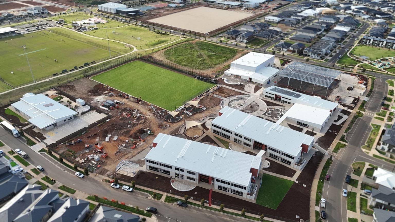 Aerial view of a school campus under construction, showing multiple new buildings, landscaped areas and surrounding residential homes.