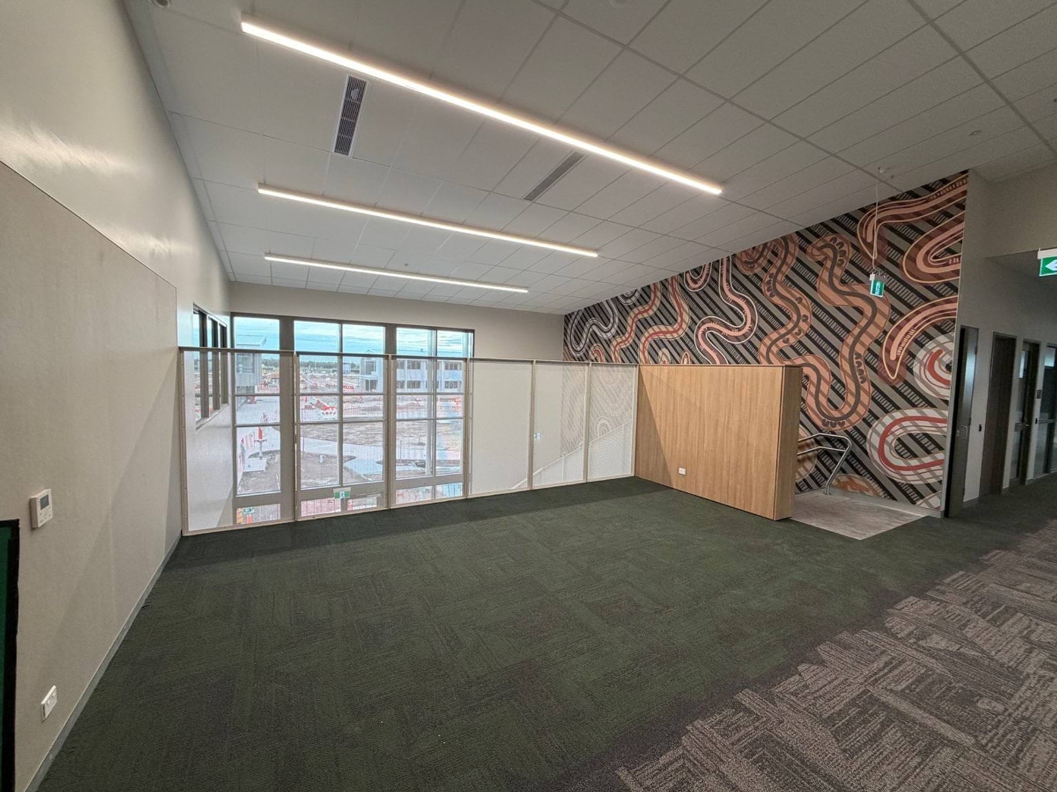 An foyer/learning area with carpet flooring, large windows and a feature wall with First Nations artwork.