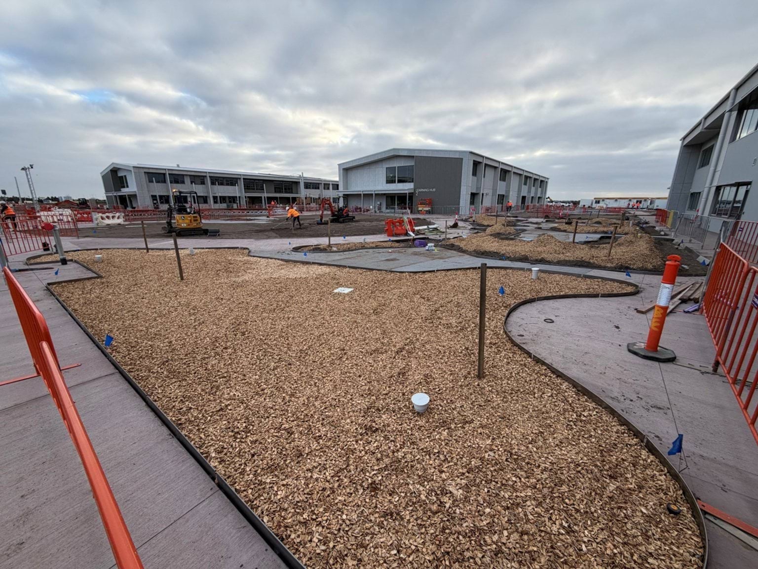 An outdoor school courtyard under construction, with landscaping works, pathways and new buildings in the background.