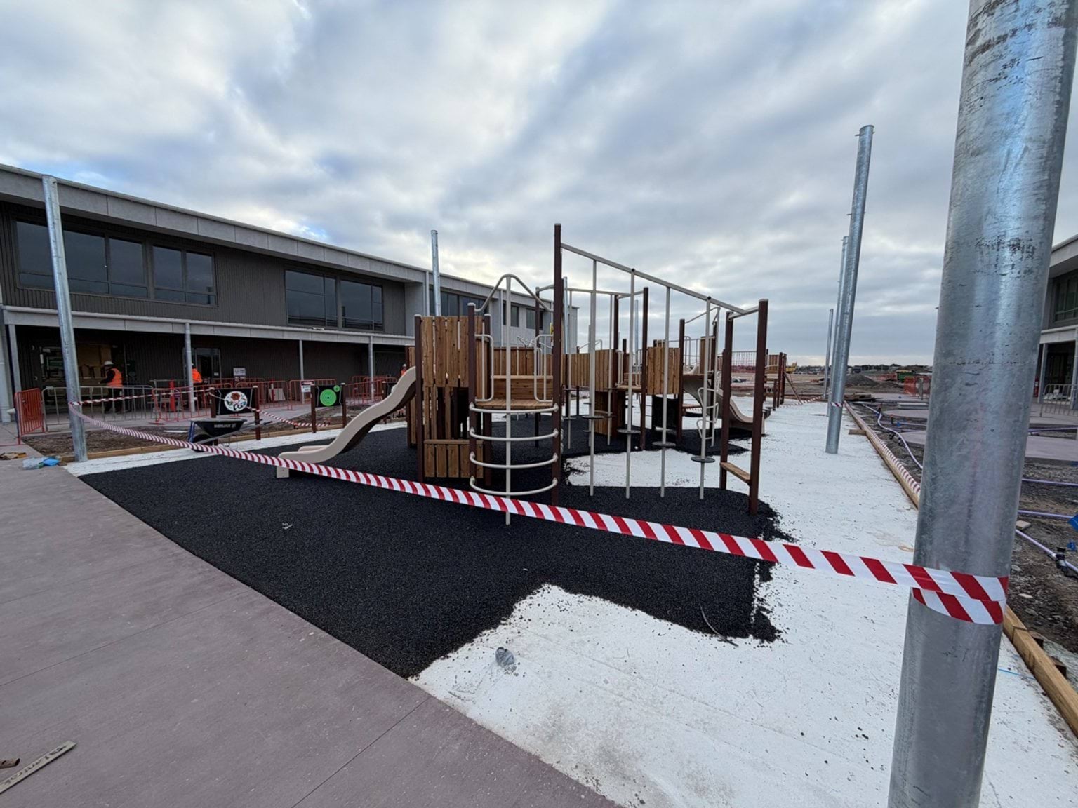 A school playground under construction, featuring new play equipment, soft-fall surfaces and surrounding outdoor learning areas.